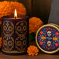 Día de los Muertos Ofrenda glass tumbler and travel tin candle featuring colorful sugar skull artwork styled in a festive marigold display for Viviana Luxury.